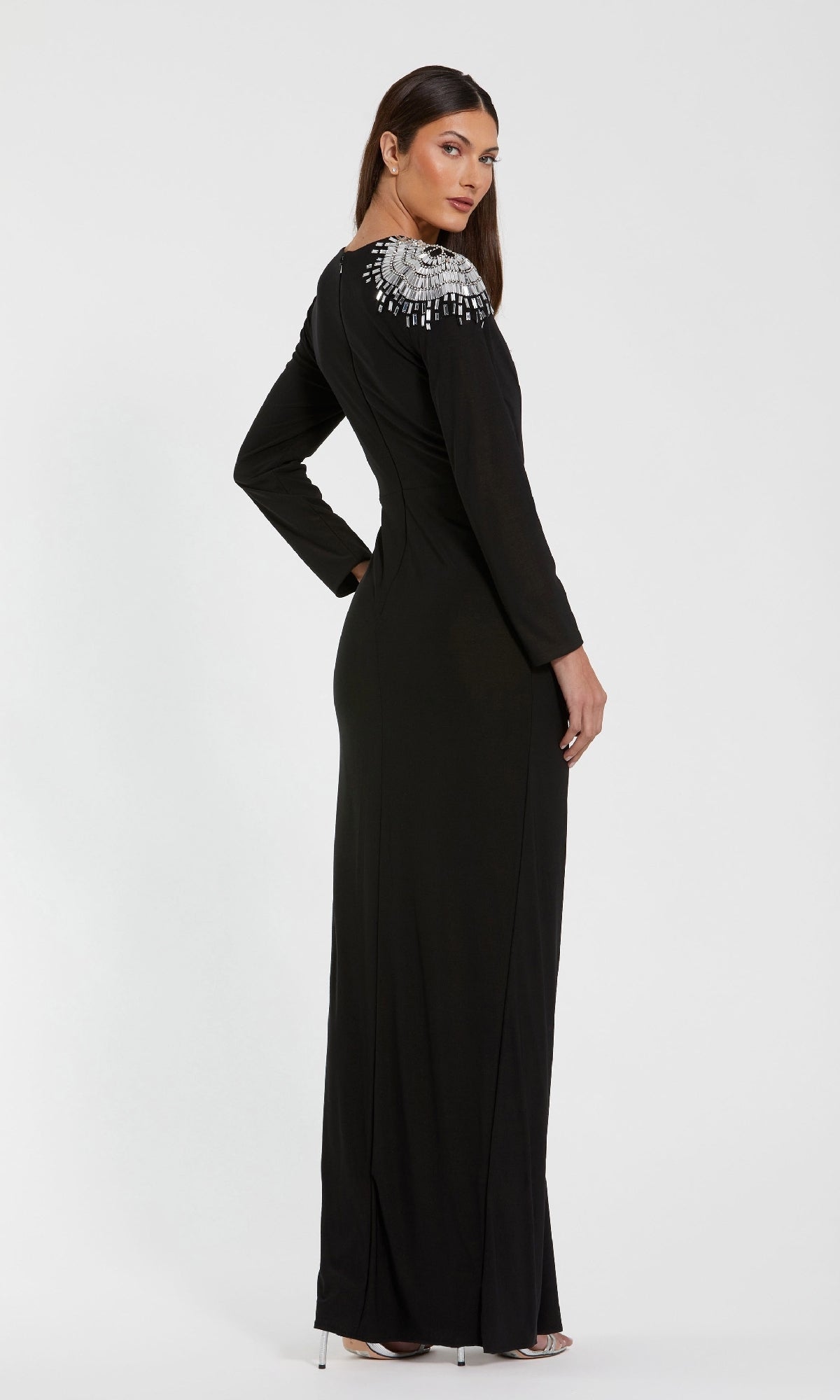 A woman stands slightly to the side against a plain background, wearing the Mac Duggal 44136 long formal dress featuring long sleeves and crystal beading on one shoulder.